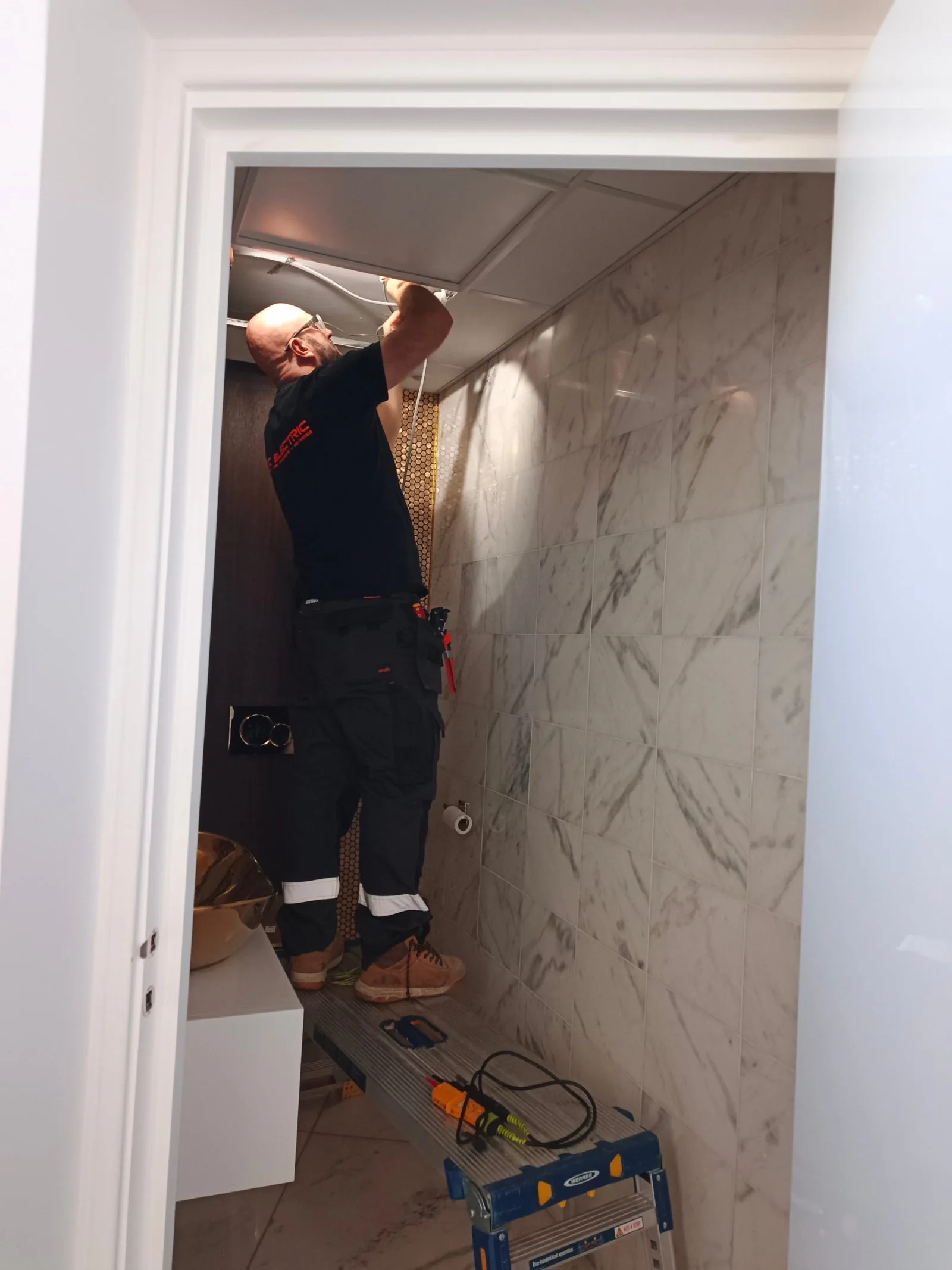 Electrician installing emergency lighting in a marble-tiled clinic WC in Poole BH14
