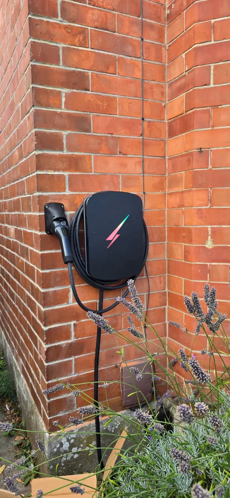 Wall-mounted EV charger with charging cable and plug holder on a brick wall in Southbourne, Bournemouth