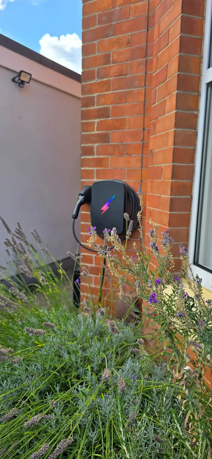Wall-mounted EV charger with cable storage seen beyond lavender on Fenton Road in Southbourne, Bournemouth