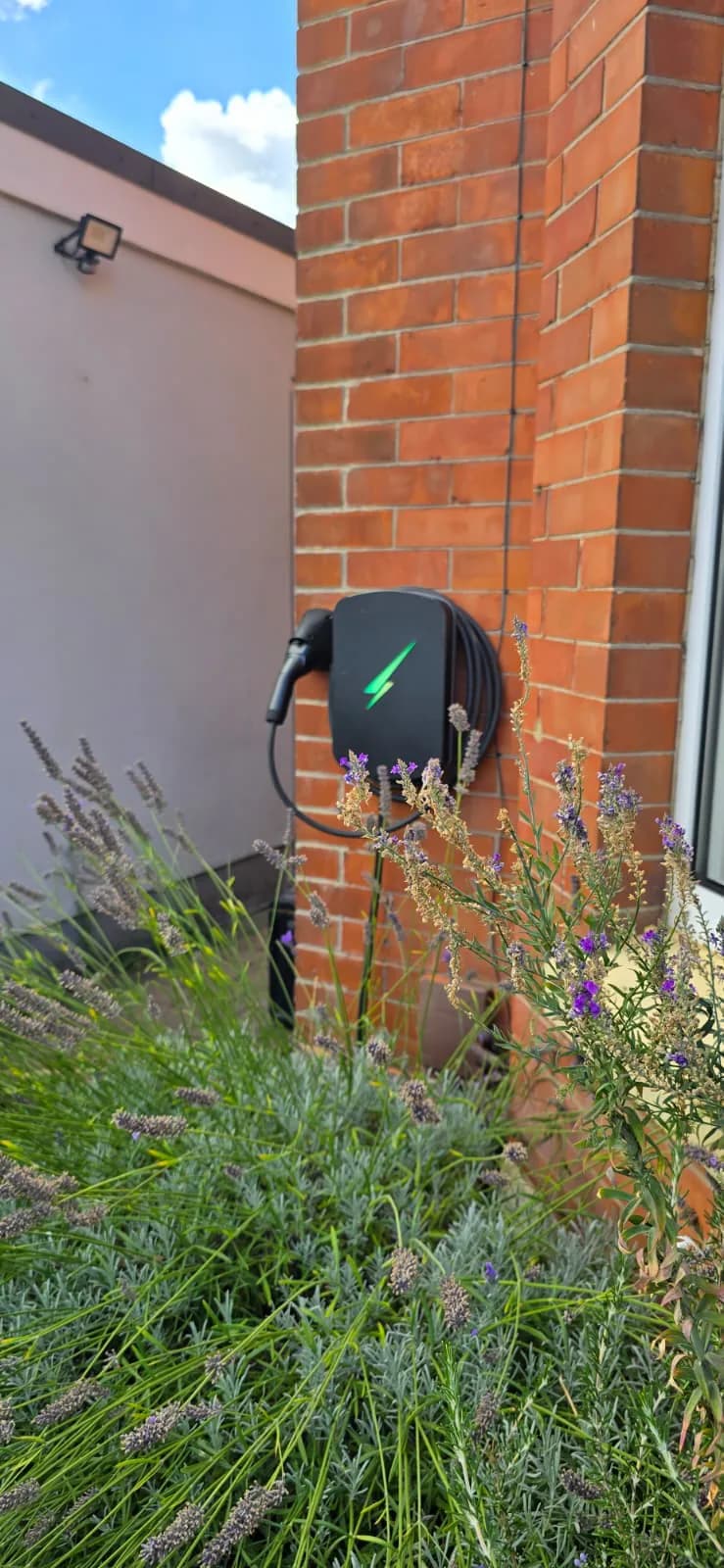 Wall-mounted EV charger with stored charging cable beside planting in Southbourne, Bournemouth