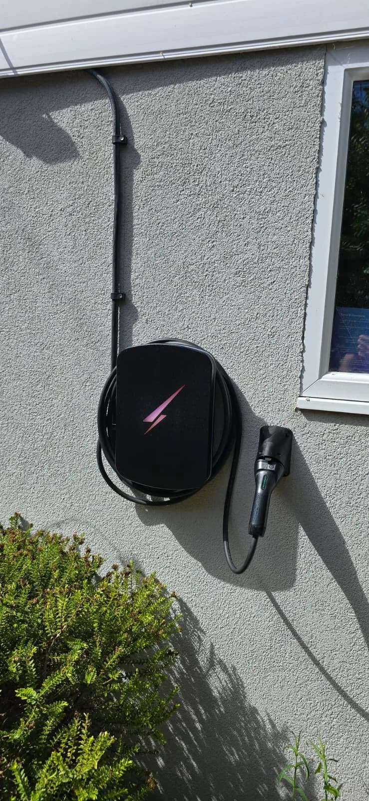 Black wall-mounted EV charger with coiled cable and plug holder on a grey rendered wall in Westbourne, Bournemouth
