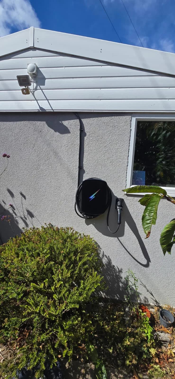 Wider view of a wall-mounted EV charger, cable storage and plug holder on a rendered wall in Westbourne, Bournemouth